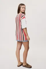 Remera oversize de manga corta con diseño de rayas verticales en tonos rojos, negros, blancos y tostados, y mangas blancas lisas.