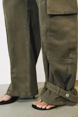Jeans cargo de tiro medio y corte barrel leg, color verde militar. Presenta bolsillos laterales con solapa en las piernas, bajo ajustable con trabilla y botón, y cierre frontal con cremallera y botón.