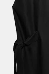 Vestido midi camisero de algodón color negro, con cuello solapa, sin mangas y cierre frontal con botones ocultos por solapa. Incluye cintura ajustable con tiras de lazada lateral en el mismo tejido.