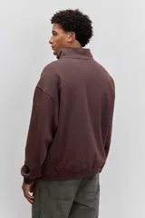 Buzo de cuello alto con cierre frontal parcial, de corte holgado y diseño minimalista con pequeño estampado central en el pecho.