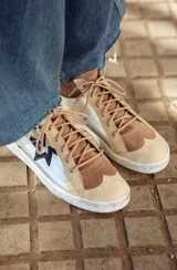 Zapatillas de cuero color beige con detalles en marrón y blanco. Aplique en forma de estrella en el lateral.