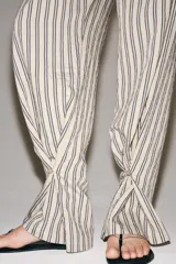 Pantalón de tiro medio con diseño de rayas verticales, confeccionado en mezcla de viscosa. Presenta cintura elástica ajustable con cordones, bolsillos laterales ocultos y pierna recta con bajo ajustable mediante botón.