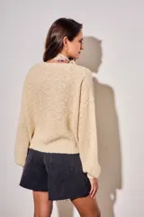 Sweater de tejido bouclé texturado color beige, con cuello redondo y mangas largas holgadas de corte amplio.