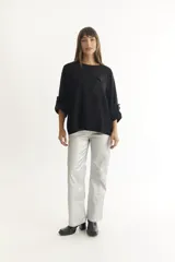 Sweater negro de tejido suave y liviano, con corte holgado, mangas 3/4 con botón decorativo y bolsillo de parche en el pecho.