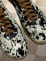 Zapatillas bajas con estampado animal print de vaca en blanco y negro, con cordones marrones y suela color caramelo.