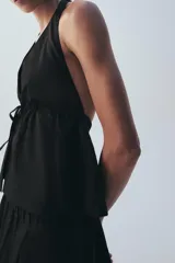 Top negro de cuello halter y escote en V pronunciado, confeccionado en popelina con frunces ajustables mediante cordón en el pecho y cierre frontal con lazada.