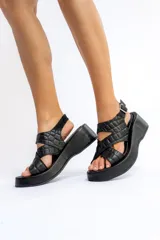 Sandalias negras de cuero con plataforma, tiras cruzadas y hebilla lateral.
