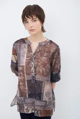 Camisa de corte recto con cuello mao y cierre frontal parcial de botones. Presenta un diseño estampado tipo patchwork con motivos florales y geométricos en tonos tierra, marrones y beige. Posee mangas tres cuartos con puños simples.