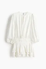 Vestido corto de color blanco en tejido con textura, con escote redondo, abertura con tiras para anudar, mangas largas abullonadas y falda de volados escalonados.