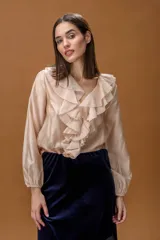 Camisa de color beige con escote en V, decorada con volados frontales y mangas largas con puños elásticos.