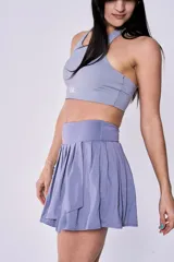 Conjunto deportivo color gris compuesto por un top de cuello alto con logo estampado y una pollera short con diseño plisado y cintura alta.