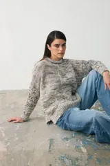 Sweater de punto con diseño jaspeado en tonos grises, cuello alto y corte holgado con mangas largas.