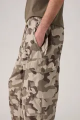 Pantalón cargo de corte amplio con estampado de camuflaje en tonos beige, marrón y verde. Cuenta con cintura elástica ajustable con cordón, bolsillos laterales con solapa y bolsillos traseros.