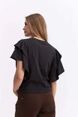 Remera negra de algodón con mangas cortas que presentan volados dobles, aportando volumen y movimiento a la prenda.