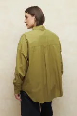 Camisa de corte clásico y holgado, confeccionada en tela blanca, con cuello camisero, cierre frontal de botones de nácar y mangas largas con puños abotonados.