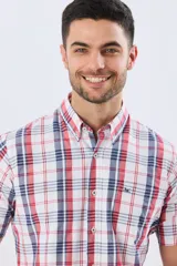 Camisa sport de manga corta con estampa de cuadros, combinando líneas rojas y azules sobre fondo blanco. Posee cuello con botones y cierre frontal abotonado.