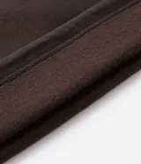 Buzo de corte holgado tipo ballon, color marrón oscuro, con cuello alto y cierre frontal parcial. Presenta mangas largas con puños elásticos y cordón ajustable en el ruedo.