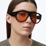 Lentes de sol estilo aviador con montura oversized de color negro y lentes polarizados en tono naranja. Presentan un diseño retro con líneas limpias y protección UV400.