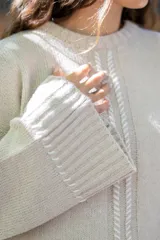 Sweater oversize de tejido de punto color beige, con cuello a la base y mangas largas acampanadas. Presenta detalles bordados a mano en color blanco en el frente, hombros y ruedo.