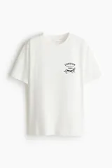 Remera oversized de punto de algodón en color blanco, con cuello redondo ribeteado, mangas cortas y un pequeño estampado gráfico frontal que dice "London Chelsea Dog Club 1998" junto a la silueta de un perro salchicha.