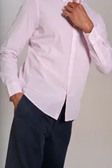Camisa de manga larga confeccionada en tejido poplin con diseño de rayas verticales finas en color rosado y blanco. Presenta cuello abotonado (button-down), cierre frontal con botones y un bolsillo en el pecho.