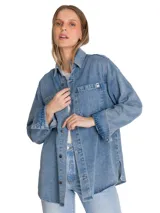 Camisa oversize de denim azul de la marca Cat, de manga larga con puños abotonados, cuello camisero y cierre frontal de botones. Presenta doble bolsillo en el pecho con etiqueta de la marca y dobladillo tipo cola de camisa.