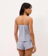 Pijama short doll de dos piezas confeccionado en algodón, con estampa de cuadros vichy en tonos azul y blanco. La musculosa presenta breteles finos, escote corazón con delicado encaje blanco y silueta fluida. El short cuenta con cintura elástica, pequeño moño frontal y terminación ondulada en el ruedo.