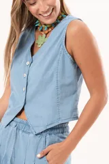 Chaleco de denim fino y liviano color celeste, con silueta entallada, escote en V y cierre frontal con botones de nácar. Presenta un diseño sastrero con terminación en puntas en la delantera.