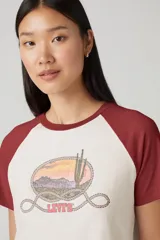 Remera estilo raglán de color crema con mangas cortas bordó. Presenta un estampado frontal de un paisaje desértico con cactus, enmarcado por una soga, y el logo "Levi's" en la parte inferior.