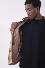 Campera tipo sobrecamisa de franela con diseño a cuadros en tonos beige y marrón. Presenta cuello clásico, cierre frontal con botones, dos bolsillos frontales con solapa y botones en el pecho, y mangas largas con puños abotonados.