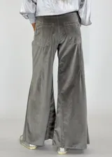 Pantalón de terciopelo gris, de corte palazzo, con bolsillos laterales y cierre frontal con botón y cremallera.