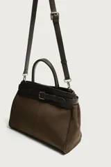 Bolso de mano estructurado en color marrón, confeccionado en una combinación de materiales que incluye gamuza en el cuerpo principal y cuero en la parte superior y asas. Presenta un detalle de cinturón decorativo con hebilla metálica plateada en la parte frontal, doble asa de mano y cierre principal con imán.