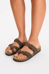 Sandalia plana de color tostado con diseño de tiras cruzadas y doble tira superior con hebillas metálicas ajustables, plantilla estilo corcho y suela negra.
