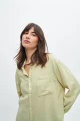 Camisa de manga larga color verde menta claro, con cuello camisero, botones frontales y un bolsillo de parche en el pecho con un pequeño bordado. Presenta un tejido con textura de rayas finas verticales.