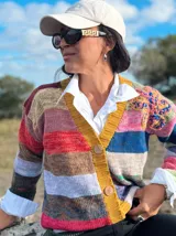 Saco de lana tejido con diseño de rayas horizontales multicolores, cuello en V con borde acanalado en color mostaza y cierre frontal con botones grandes. Presenta un detalle bordado en relieve en la parte superior delantera y mangas largas.