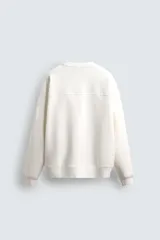 Sudadera negra de corte relaxed fit, confeccionada en tejido técnico interlock de algodón con elasticidad. Presenta cuello redondo, manga larga y una etiqueta aplicada en el bajo. Los acabados son en rib.