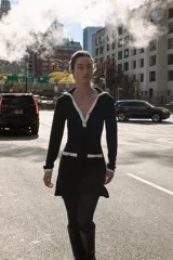 Vestido corto de tejido suave, color negro con detalles en blanco. Presenta cuello solapa, escote en pico, manga larga, falsos bolsillos delanteros y cierre frontal con botones dorados.