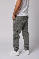 Pantalón jean gris claro, estilo jogger, con bolsillos cargo laterales y puños elásticos en los tobillos.