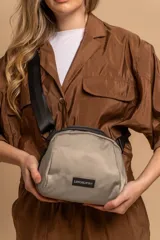 Bandolera pequeña de diseño moderno, confeccionada en tafeta liviana y resistente. Cuenta con cierre superior, correa ancha ajustable y logo frontal de la marca.