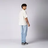 Remera oversize de lino entramado color blanco off-white, con cuello redondo, mangas cortas de hombro caído y etiqueta aplicada en el borde inferior.