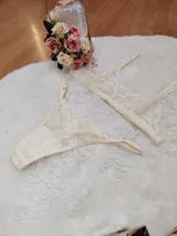 Conjunto de lencería de encaje color champagne, compuesto por un bralette triangular sin aro y una bombacha tipo tanga con tiras laterales ajustables.