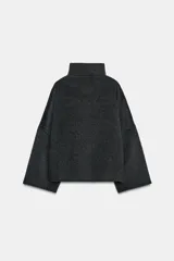 Cazadora de corte amplio confeccionada en hilatura con lana, color beige. Presenta cuello subido, manga larga y cierre frontal con botones negros. Destaca por sus acabados con costuras de hilo a contraste en los bordes.