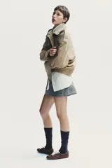 Cazadora de mujer confeccionada en piel de ante color gris oscuro con cuello subido, manga larga con trabillas en los hombros, bolsillos delanteros y con solapa en el pecho. Cierre frontal con cremallera y solapa con botones a presión.