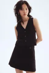 Chaleco negro, corto, con escote en V pronunciado y cierre frontal de tres botones oscuros. Presenta pinzas moldeadoras para un calce entallado y está forrado.