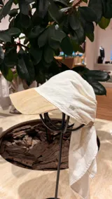 Gorro tipo pañuelo con visera rígida negra, confeccionado en lino color beige con finas rayas verticales oscuras.