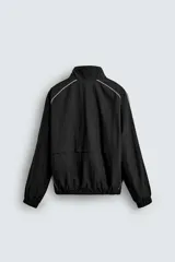 Chaqueta técnica de corte relajado en color verde oscuro, con cuello subido, cierre frontal de cremallera y detalles de líneas en contraste. Presenta bolsillos frontales con cremallera oculta y acabados elásticos en puños y ruedo.
