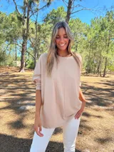 Buzo oversize color beige con cuello redondo, manga larga y corte asimétrico en el bajo.