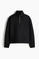 Buzo negro de tejido pesado con efecto neopreno, cuello elevado y medio cierre frontal plateado. Presenta hombros caídos, mangas largas y puños y bajo acanalados.