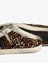 Zuecos Golden Goose modelo Super-Star Sabot, con diseño de zapatilla sin talón. Presentan exterior cubierto de glitter negro y dorado, estrella característica en el lateral, cordones y forro interior de shearling sintético.