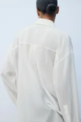 Camisa oversize blanca de cuello solapa y manga larga con puños anchos. Cuenta con cierre frontal de botones y un bolsillo aplicado en el frente.